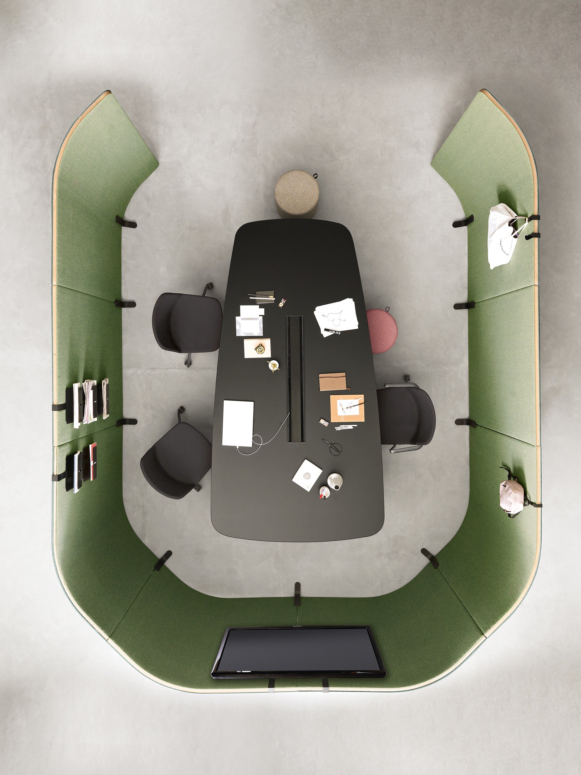 Vue aérienne d'un espace de réunion moderne meublé avec le Mobilier de direction Pigreco d'Attitudes Bureaux : table noire, quatre chaises, tabouret rouge, cahiers, ordinateurs portables - un espace élégant avec un pare-vue vert, des étagères et un écran mural.