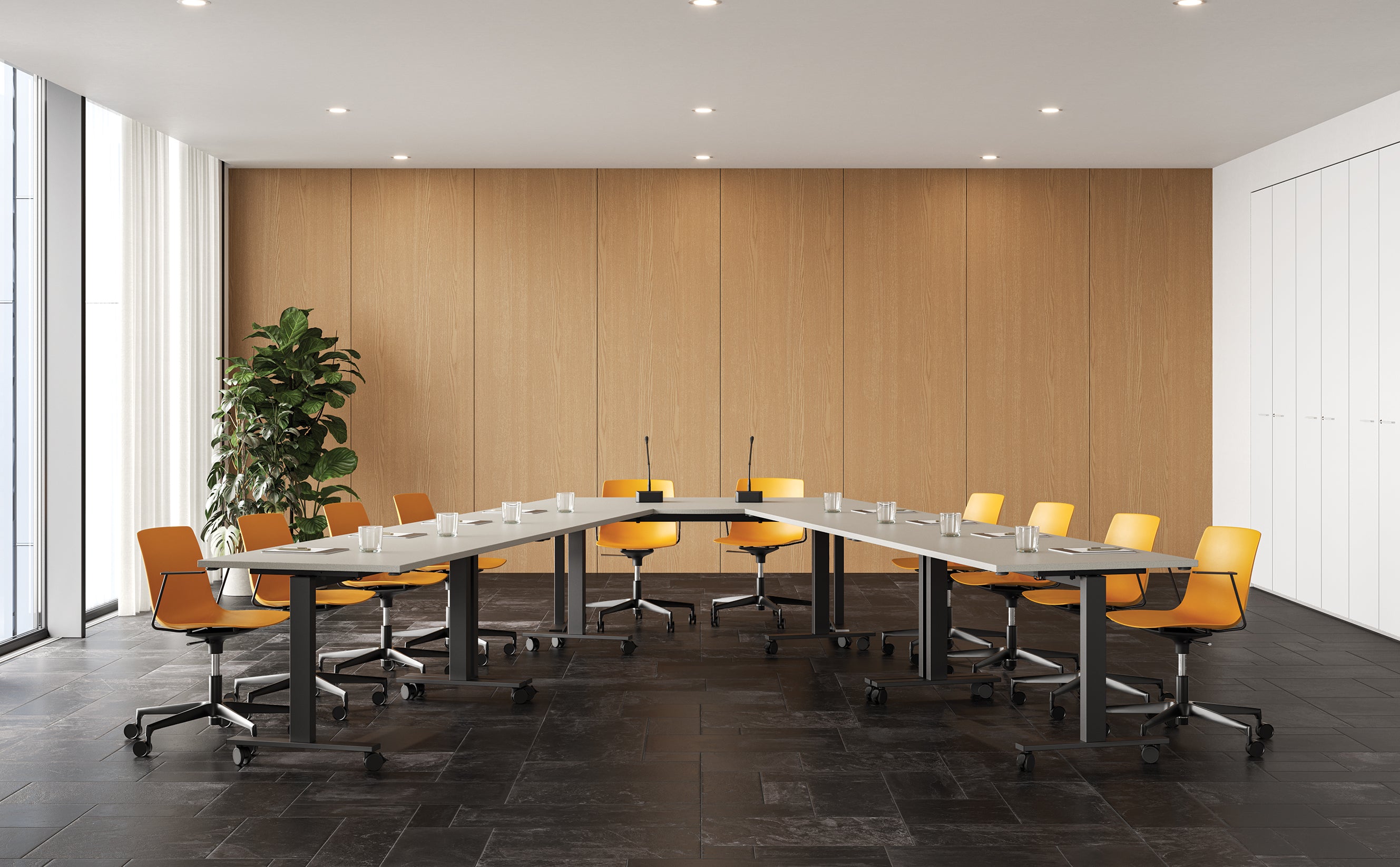 Salle de conférence moderne équipée de la Pop Folding table de réunion pliante sur roulettes d'Attitudes Bureaux, de plusieurs chaises jaunes sur roulettes, de verres d'eau, de blocs-notes, de microphones, d'une plante en pot, de murs lambrissés et de grandes fenêtres avec lumière naturelle.