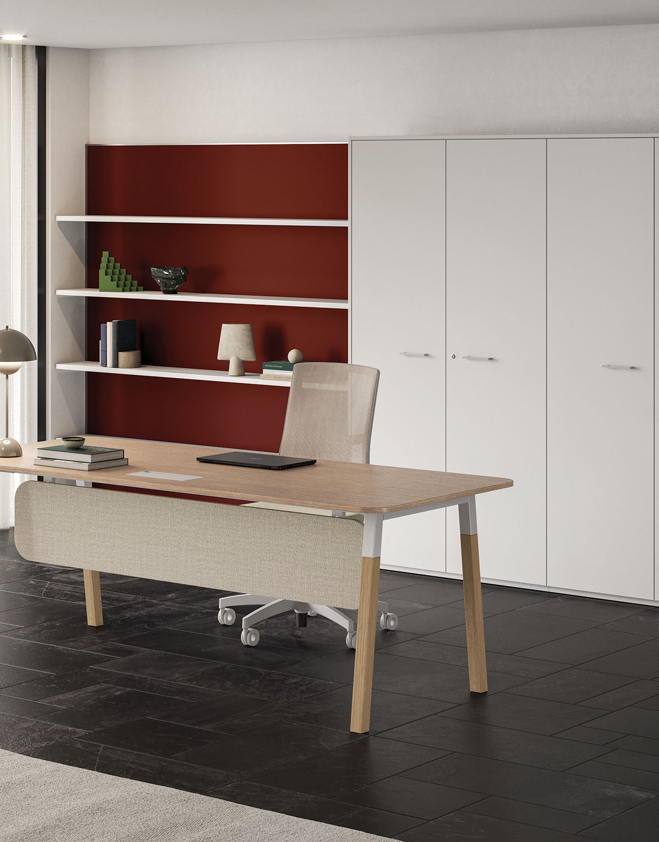 Un bureau moderne avec un bureau en bois, une chaise beige et des étagères ouvertes se trouve contre un mur d'accent rouge. Sur la droite, Attitudes Bureaux Armoires de bureau Passepartout et des armoires blanches offrent un espace de rangement. Une lampe décore le bureau.