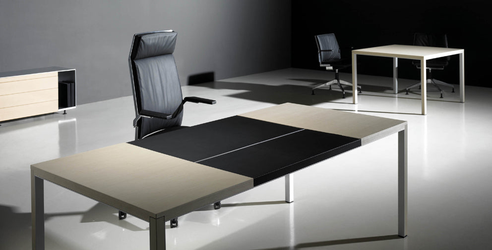 Un bureau moderne et minimaliste avec deux bureaux Neta Executive d'Attitudes Bureaux et trois chaises noires sous des lumières vives ; le bureau principal comporte des finitions nobles, le tout sur un mur gris foncé et un sol clair pour un espace de travail contemporain.